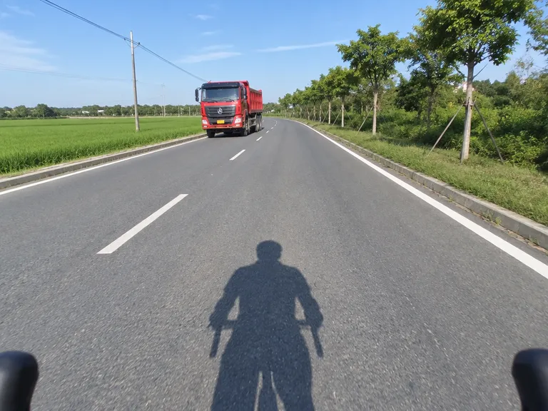 Opening frame of an impossible cycling POV: sunlit shadow and distant red dump truck